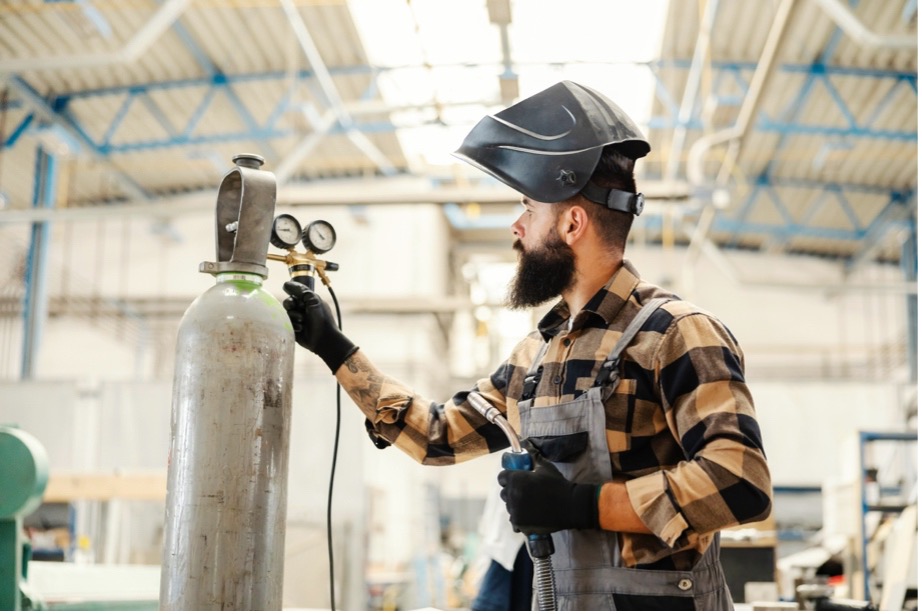 A person wearing a welding mask and holding a gas cylinder
