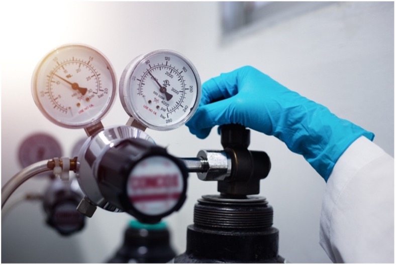 A person in a lab coat and gloves holding a pressure gauge