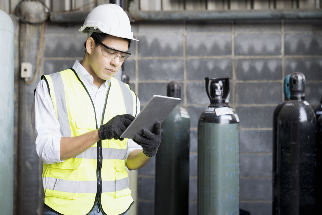 Male heavy industrial worker using a digital tablet inside manufacturing. Acetylene and oxygen gas steel storage tanks for welding.