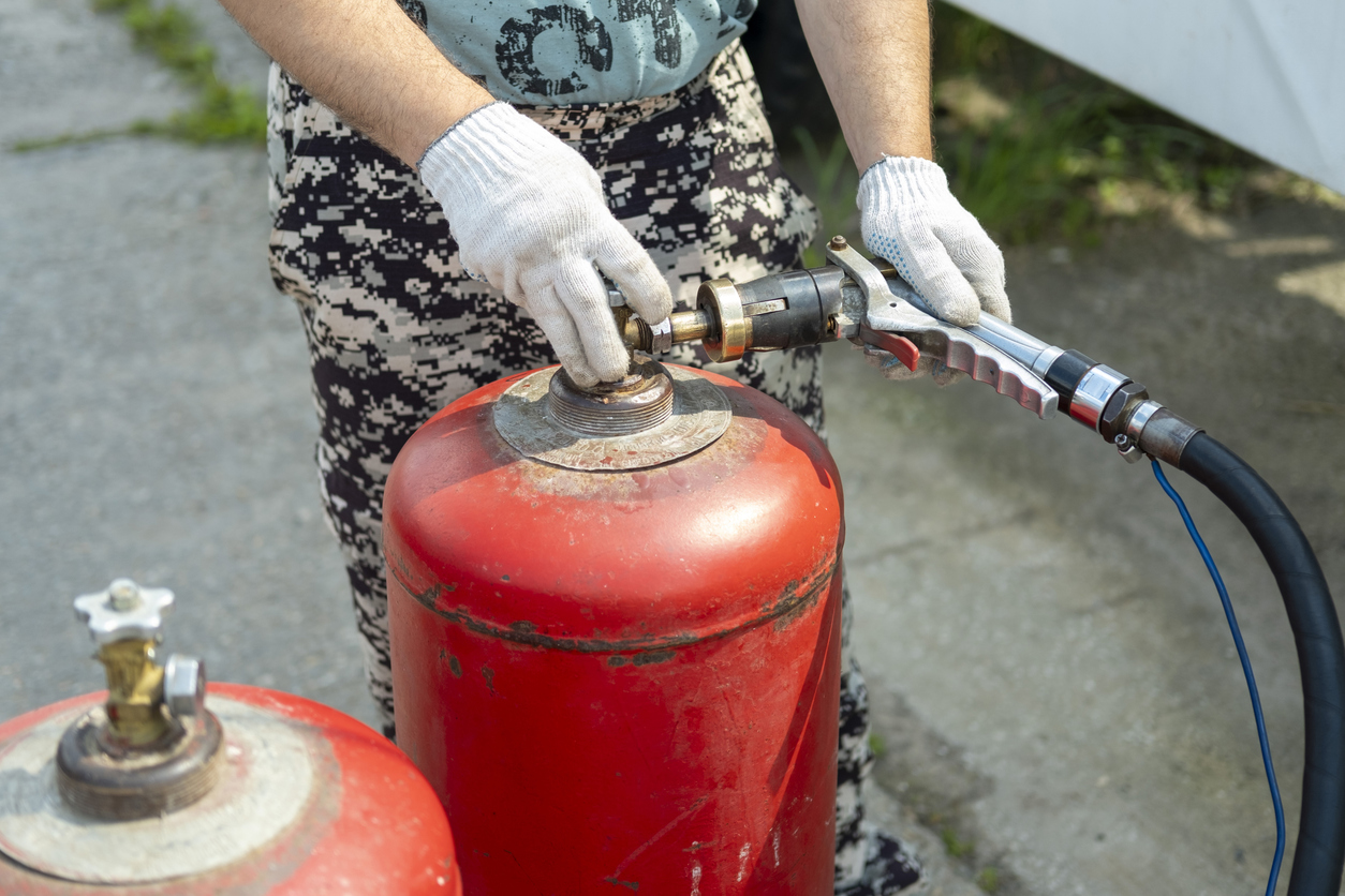 A person connects the gas supply hose. Gas cylinder filling process. A gas cylinder is designed for transportation and storage of liquefied hydrocarbon gases, propane, butane and their mixtures.