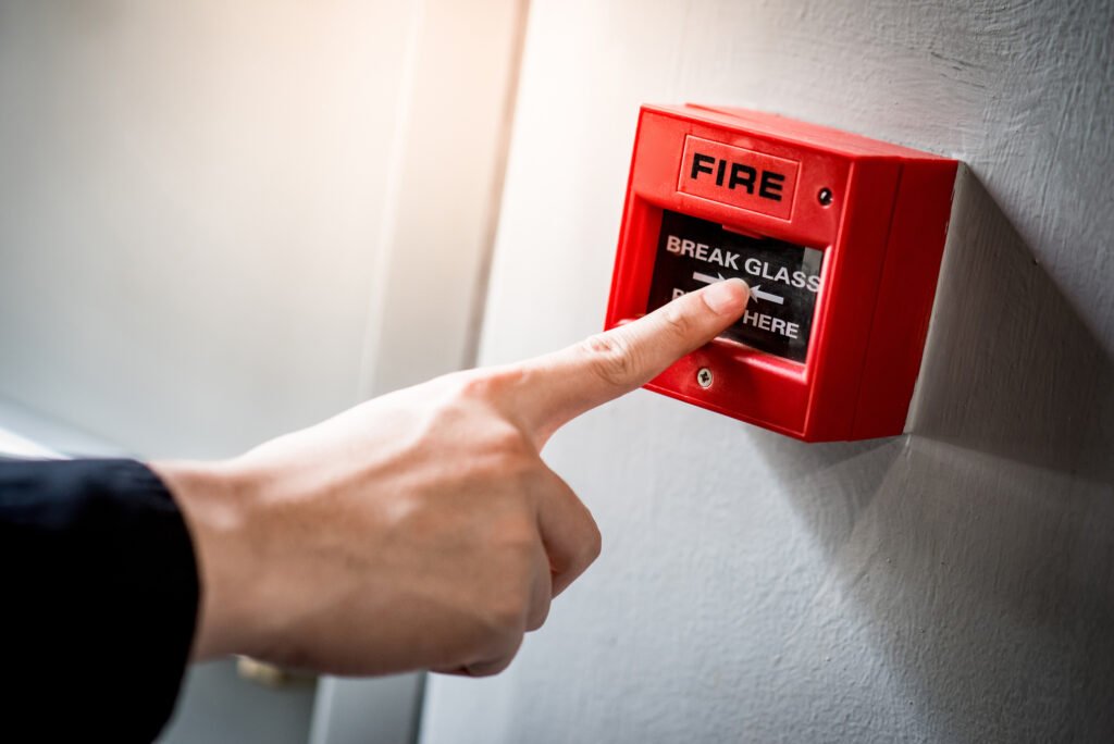 hand pointing at red fire alarm switch on concrete wall in office building. Industrial fire warning system equipment for emergency.